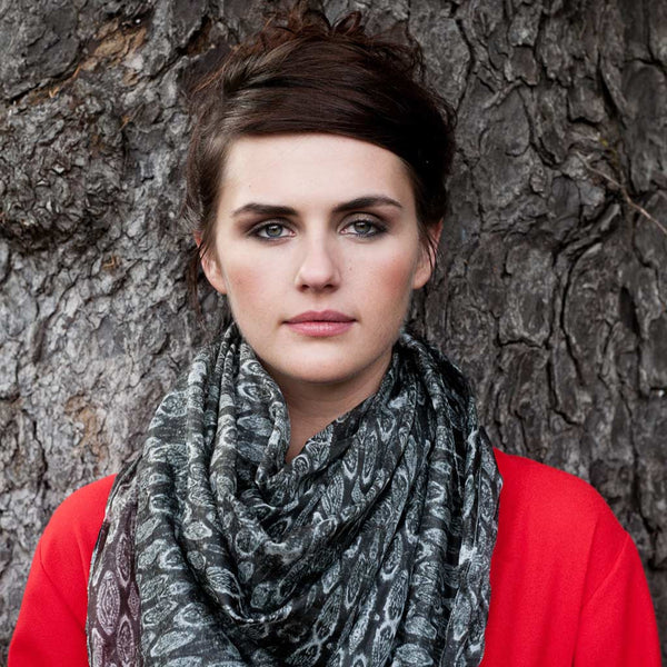 Carley Kahn "Ngawha Springs" silk scarf. Model in red shirt wears scarf around neck while leaning against tree. 