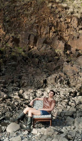Carley Kahn "Checker" upholstery fabric. Model reclining in upholstered chair on rocky beach against rocky cliff backdrop. 