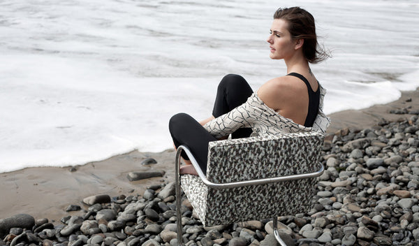 Carley Kahn "Scallop" upholstery fabric. Model sits in upholstered chrome chair with back to us. On beach close to water. 