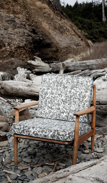 Carley Kahn "Stripe" upholstery fabric. Upholstered chair in black and white colorway on rocky beach. 