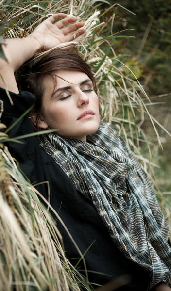 Carley Kahn "Abel Tasman" silk scarf on model, dressed in black and reclining against a grassy hill with her eyes closed. 